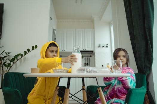 Two kids in pajamas sit at a table enjoying breakfast with milk in a cozy kitchen setting.